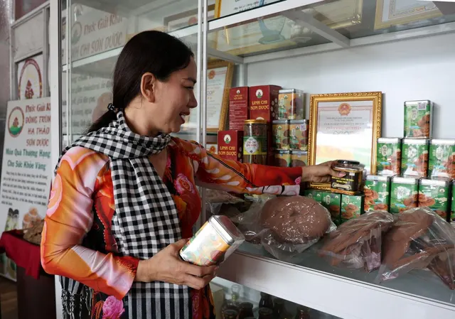 Chị Nương quàng khăn rằn, xem một hộp sản phẩm bên quầy trưng bày nấm linh chi