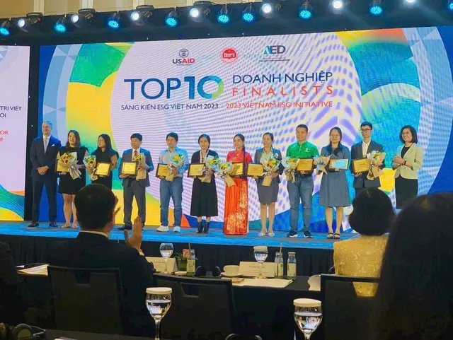 Mười đại diện doanh nghiệp đứng thành hàng trên sân khấu, cầm hoa và chứng nhận, chị Châu Thị Nương mặc áo dài đỏ ở giữa; màn hình phía sau ghi Top 10 doanh nghiệp Finalists, Sáng kiến ESG Việt Nam 2023, cùng logo USAID