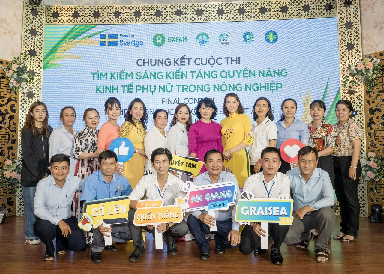 Các thí sinh và khách mời chụp ảnh chung trước phông chung kết, cầm bảng cổ vũ có chữ An Giang và GRAISEA