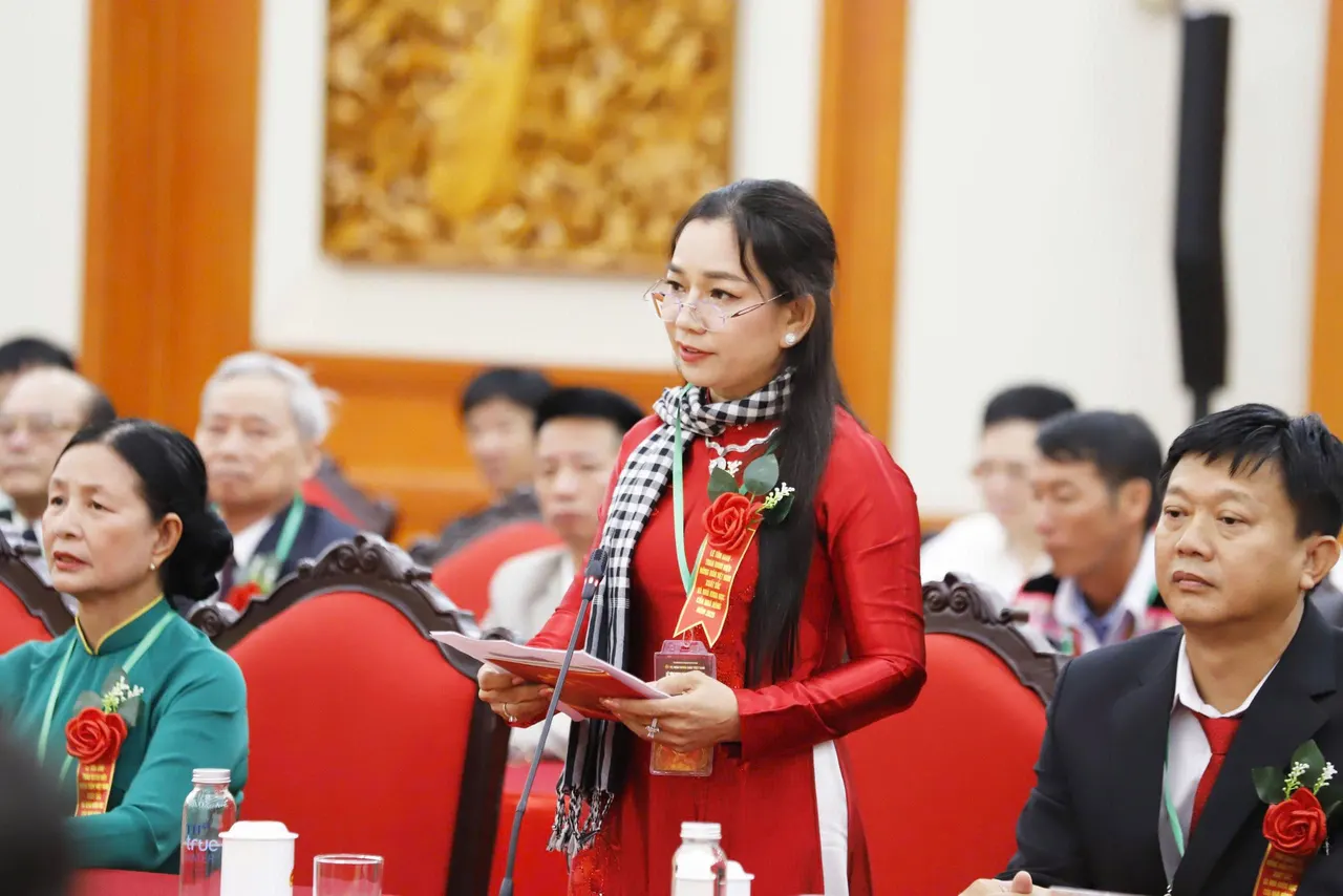 Chị Châu Thị Nương mặc áo dài đỏ, quàng khăn rằn, cài hoa đỏ trên ngực, đứng phát biểu giữa hội trường