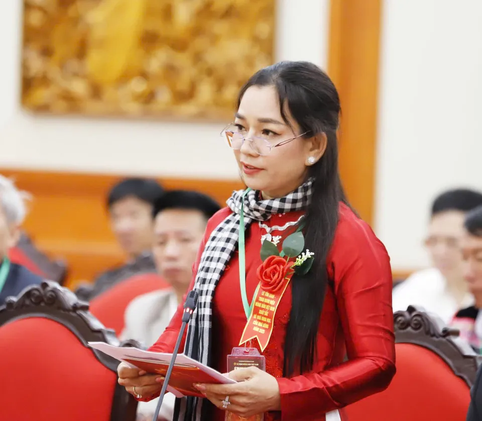 Chị Châu Thị Nương mặc áo dài đỏ, quàng khăn rằn, đứng cầm tài liệu phát biểu trước micro tại một buổi lễ